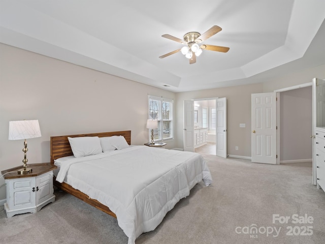 carpeted bedroom with ceiling fan, ensuite bathroom, and a raised ceiling