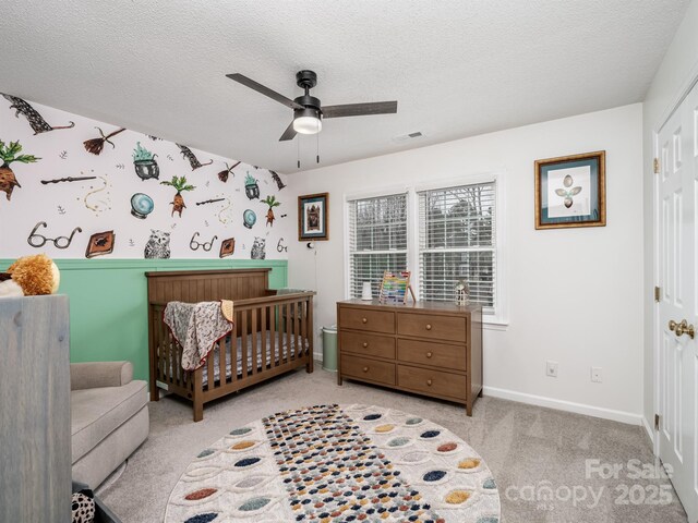 bedroom with a textured ceiling, ceiling fan, a closet, a nursery area, and light colored carpet