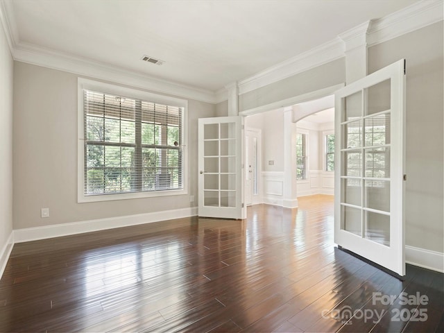 empty room featuring dark hardwood / wood-style floors, ornate columns, ornamental molding, and french doors