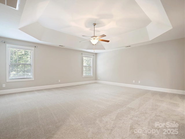 carpeted spare room featuring a raised ceiling, plenty of natural light, and ceiling fan