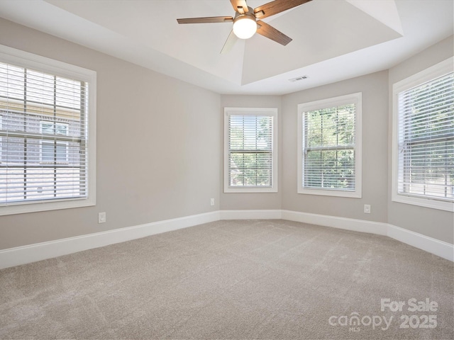 carpeted empty room with a raised ceiling and ceiling fan