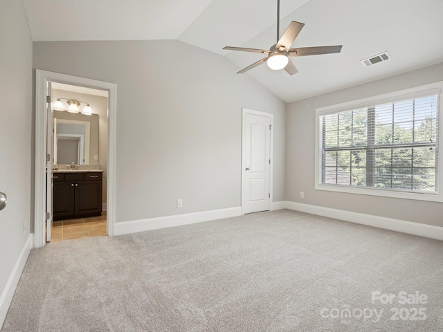 unfurnished bedroom with ensuite bath, ceiling fan, light carpet, and vaulted ceiling