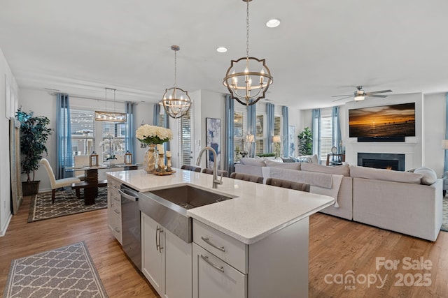 kitchen featuring white cabinetry, hanging light fixtures, dishwasher, a kitchen island with sink, and ceiling fan with notable chandelier