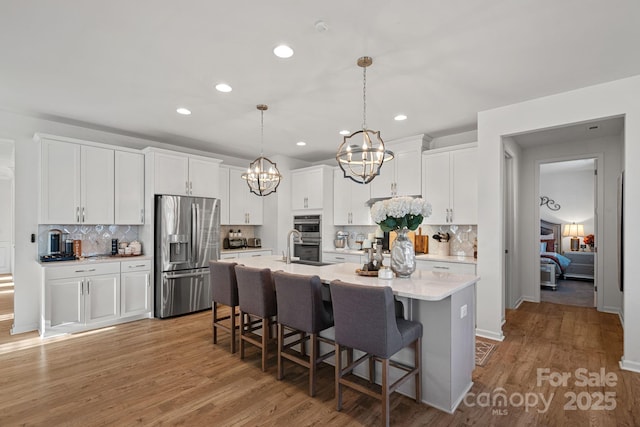 kitchen with an island with sink, appliances with stainless steel finishes, white cabinets, and light countertops