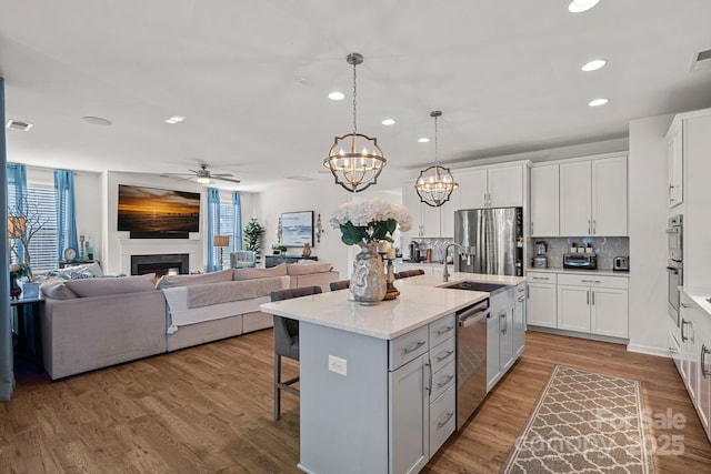 kitchen with decorative light fixtures, stainless steel appliances, open floor plan, white cabinets, and a kitchen island with sink