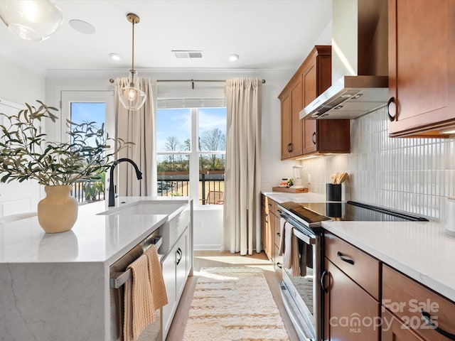 kitchen with brown cabinets, stainless steel appliances, tasteful backsplash, a sink, and wall chimney exhaust hood