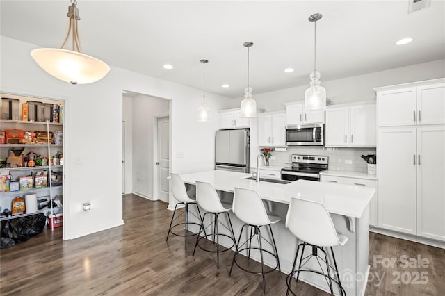 kitchen featuring decorative light fixtures, stainless steel appliances, an island with sink, and sink