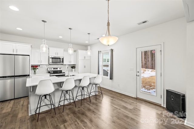 kitchen with decorative light fixtures, a center island with sink, tasteful backsplash, white cabinets, and appliances with stainless steel finishes