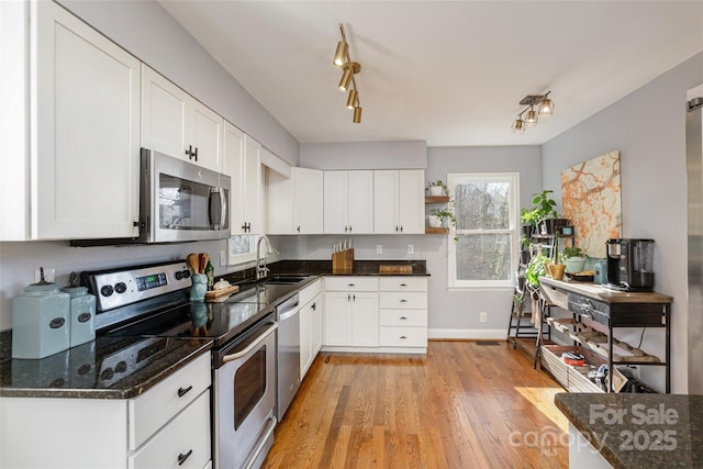 kitchen featuring white cabinetry, sink, dark stone counters, appliances with stainless steel finishes, and light wood-type flooring