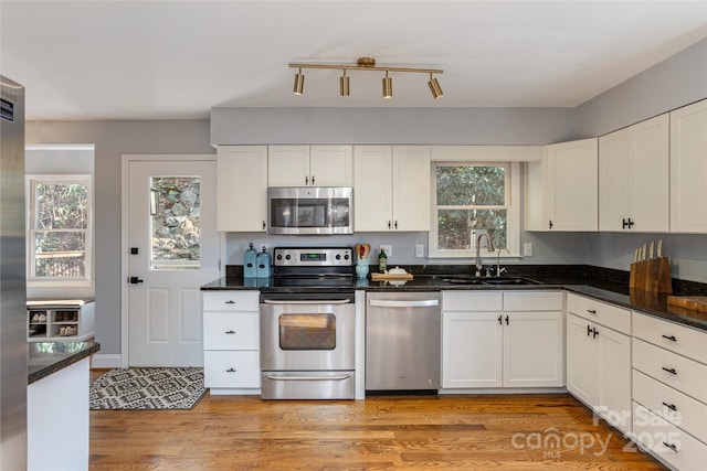 kitchen with stainless steel appliances, sink, light hardwood / wood-style flooring, dark stone countertops, and white cabinetry