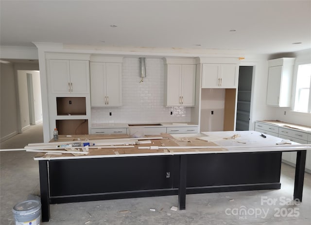 kitchen featuring backsplash, a kitchen island, concrete flooring, and white cabinets