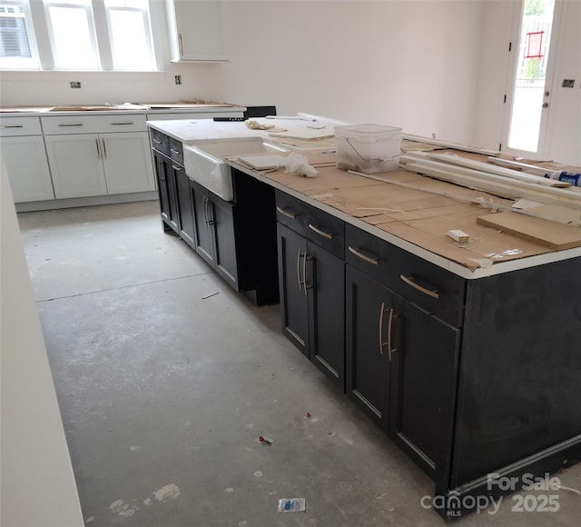 kitchen featuring concrete flooring, dark cabinets, white cabinets, and light countertops