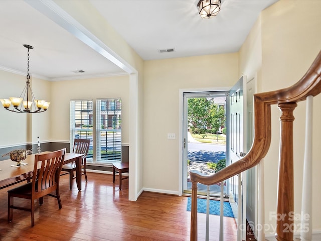 foyer entrance with wood-type flooring, crown molding, and an inviting chandelier