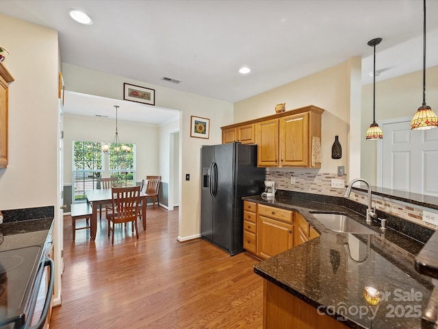 kitchen with sink, black fridge, hanging light fixtures, and dark stone counters