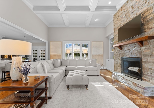 living room featuring built in shelves, a stone fireplace, coffered ceiling, ornamental molding, and beamed ceiling