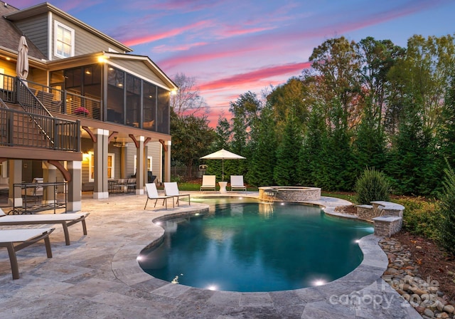 pool at dusk with an in ground hot tub, a sunroom, and a patio area