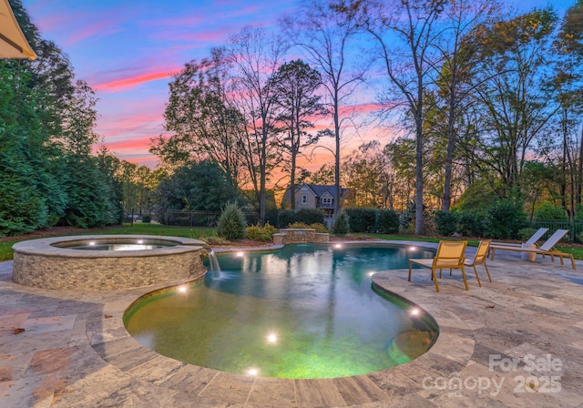 pool at dusk with an in ground hot tub, pool water feature, and a patio