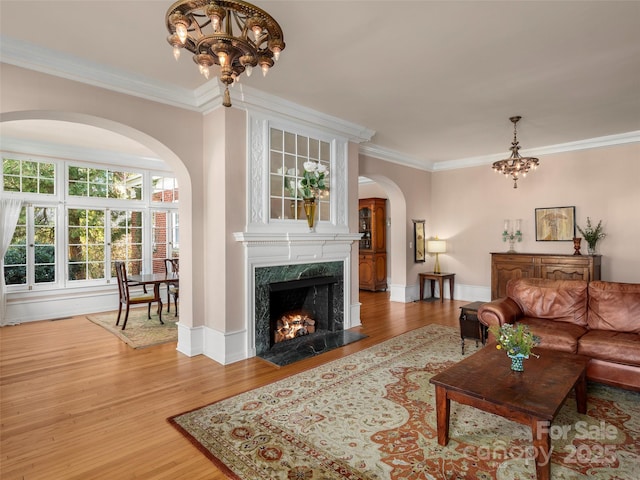 living room with crown molding, an inviting chandelier, a high end fireplace, and hardwood / wood-style flooring