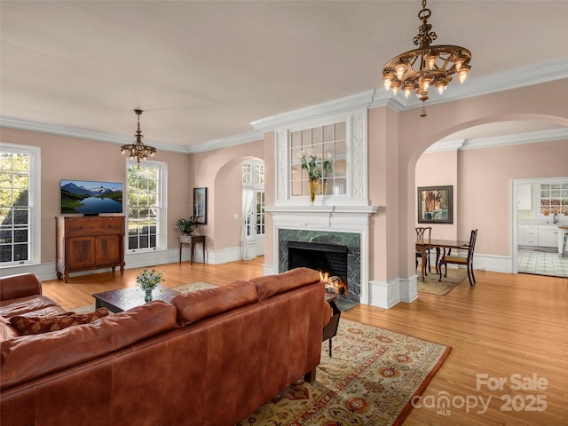 living room featuring a notable chandelier, light wood-type flooring, ornamental molding, and a premium fireplace