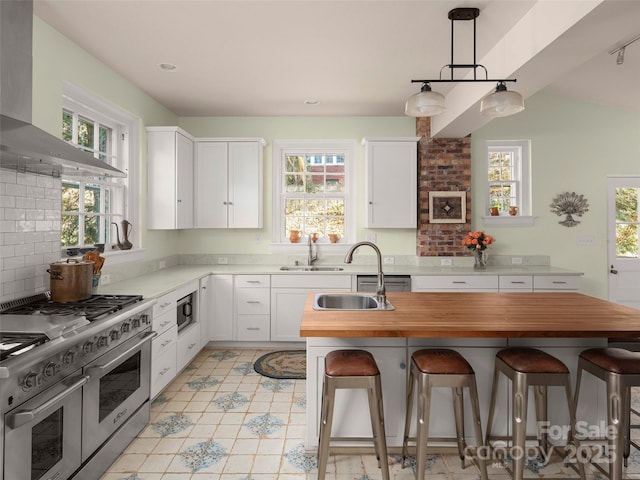 kitchen with wall chimney exhaust hood, hanging light fixtures, a kitchen breakfast bar, white cabinets, and appliances with stainless steel finishes