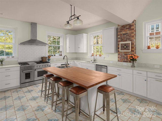 kitchen featuring white cabinets, wall chimney range hood, sink, an island with sink, and stainless steel appliances