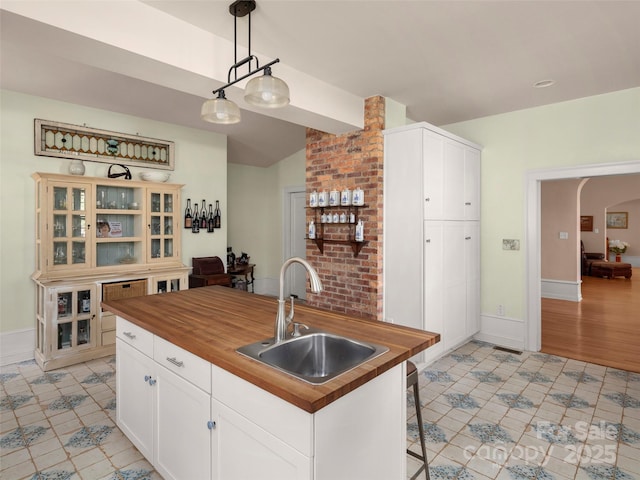 kitchen with sink, wood counters, decorative light fixtures, a kitchen island with sink, and white cabinets