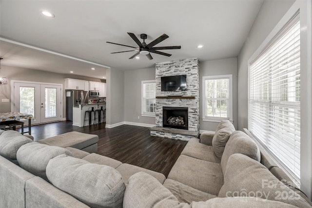 living room featuring a fireplace, a healthy amount of sunlight, ceiling fan with notable chandelier, and dark wood-type flooring