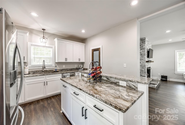 kitchen with stainless steel appliances, a kitchen island, sink, white cabinetry, and hanging light fixtures