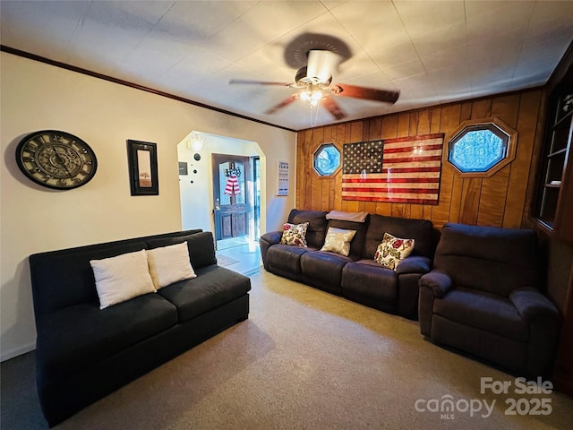 living room with carpet flooring, wood walls, ceiling fan, and ornamental molding