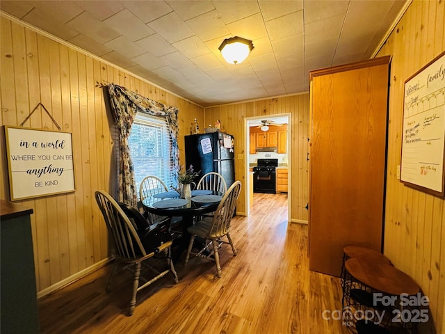 dining room featuring light hardwood / wood-style flooring, ceiling fan, and wood walls