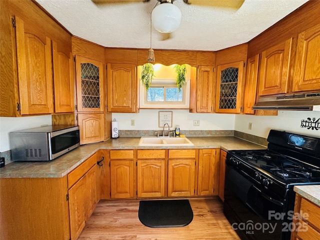 kitchen featuring sink, black gas stove, pendant lighting, light hardwood / wood-style floors, and a textured ceiling