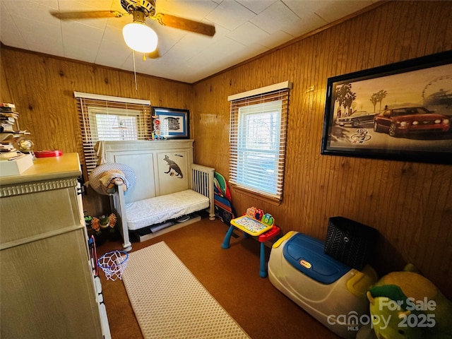 carpeted bedroom with ceiling fan, ornamental molding, and wood walls