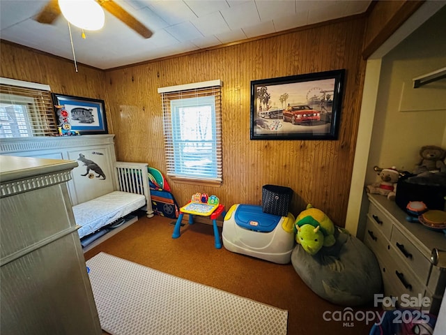 carpeted bedroom with ceiling fan, wood walls, and ornamental molding