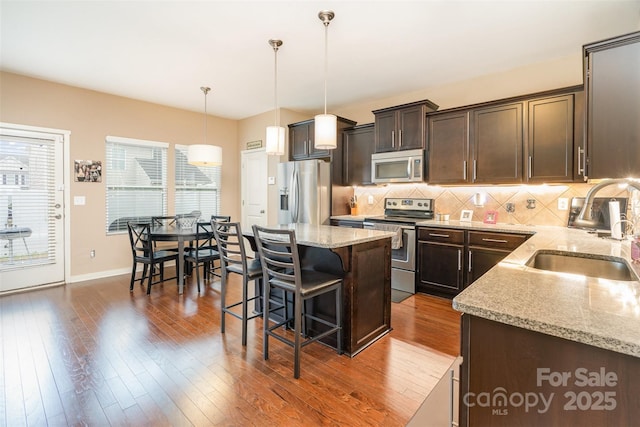 kitchen with sink, hanging light fixtures, stainless steel appliances, dark brown cabinets, and a kitchen island