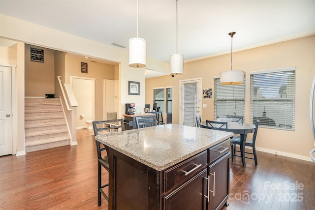 kitchen featuring dark hardwood / wood-style flooring, dark brown cabinetry, decorative light fixtures, a kitchen island, and a breakfast bar area