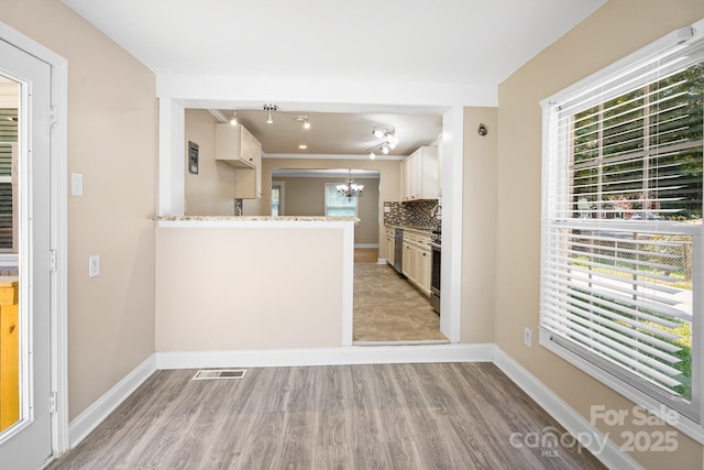 kitchen featuring decorative backsplash, kitchen peninsula, light stone counters, white cabinetry, and plenty of natural light