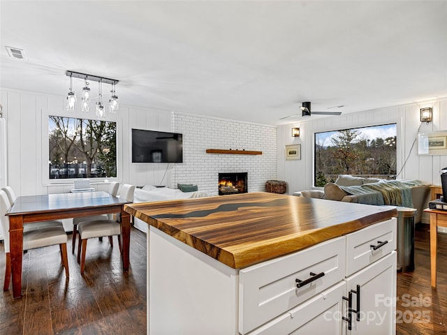 kitchen with a kitchen island, ceiling fan, a fireplace, butcher block countertops, and white cabinetry