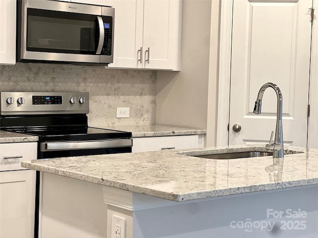 kitchen with sink, light stone counters, appliances with stainless steel finishes, decorative backsplash, and white cabinets