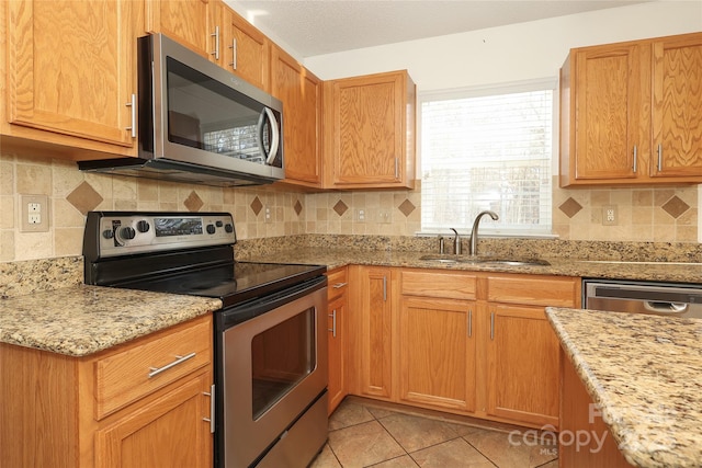 kitchen featuring appliances with stainless steel finishes, tasteful backsplash, light stone counters, sink, and light tile patterned floors