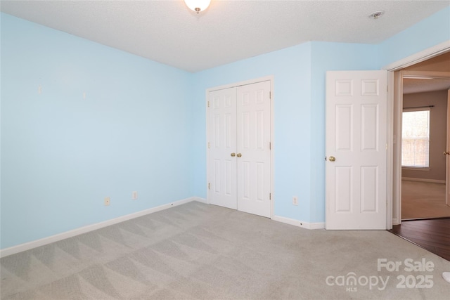 unfurnished bedroom featuring a textured ceiling, light colored carpet, and a closet