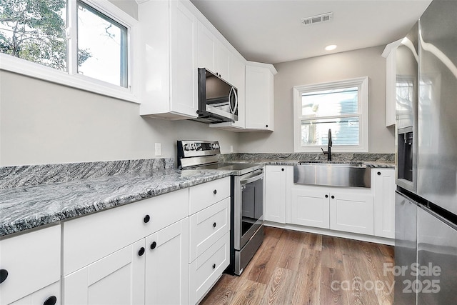 kitchen featuring sink, white cabinetry, stainless steel appliances, dark hardwood / wood-style flooring, and light stone counters