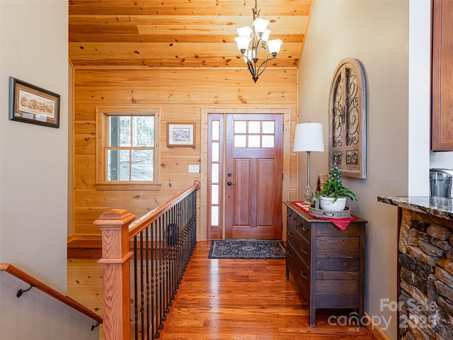 foyer entrance with vaulted ceiling, wooden walls, wooden ceiling, a chandelier, and light hardwood / wood-style floors