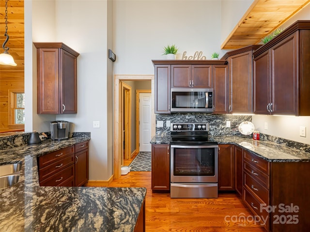 kitchen featuring pendant lighting, dark hardwood / wood-style flooring, dark stone countertops, and appliances with stainless steel finishes