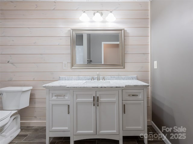 bathroom featuring vanity, toilet, and wooden walls