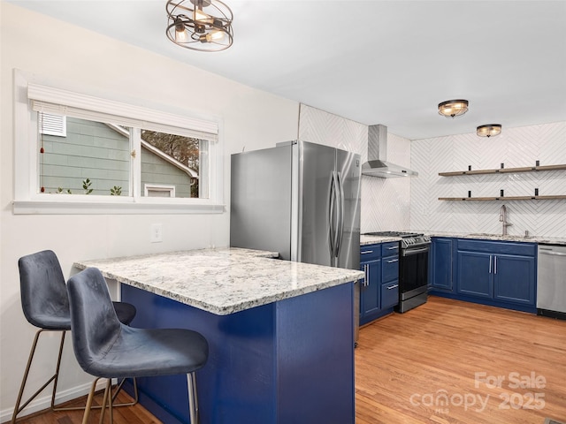 kitchen featuring sink, wall chimney exhaust hood, blue cabinets, decorative backsplash, and appliances with stainless steel finishes