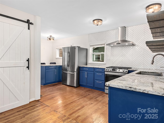 kitchen with appliances with stainless steel finishes, wall chimney exhaust hood, sink, blue cabinetry, and a barn door