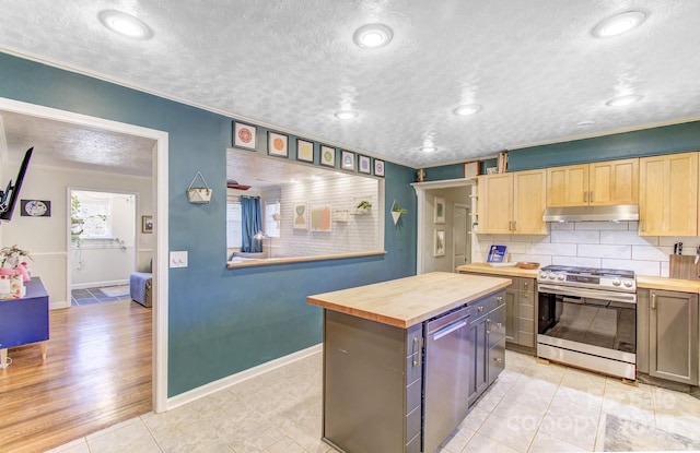 kitchen featuring under cabinet range hood, wood counters, appliances with stainless steel finishes, backsplash, and light brown cabinetry