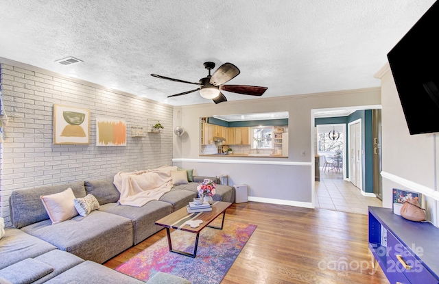 living room featuring ceiling fan, a textured ceiling, brick wall, wood finished floors, and baseboards