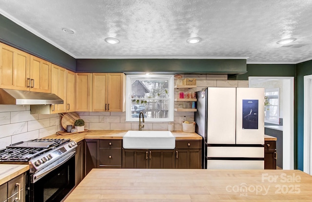 kitchen featuring wood counters, stainless steel range with gas stovetop, freestanding refrigerator, under cabinet range hood, and a sink