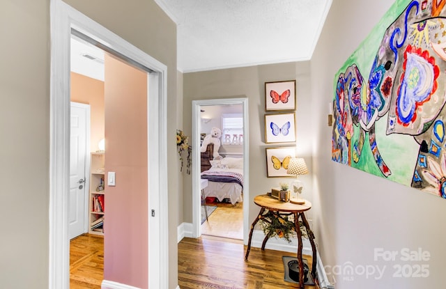 hall with baseboards, a textured ceiling, visible vents, and wood finished floors